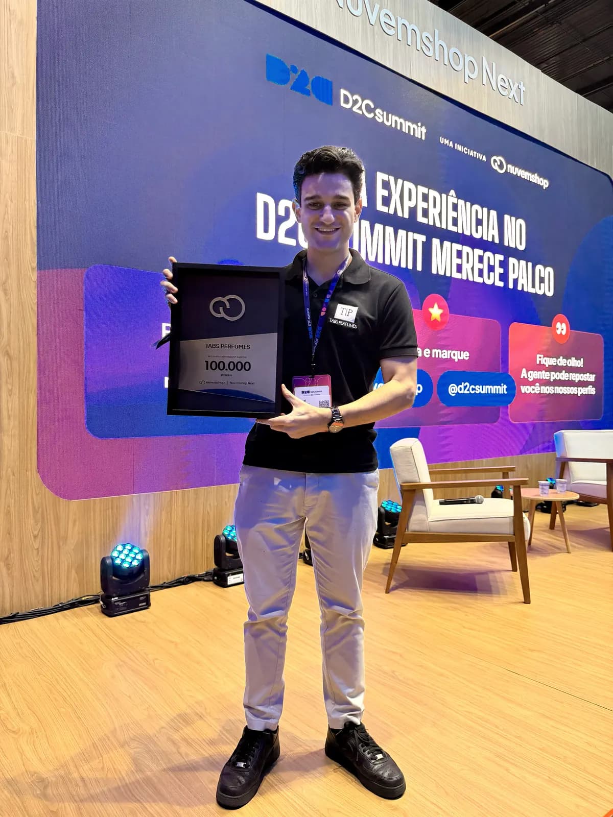 Gabriel Tabchoury, fundador da Tabs, segurando a placa da Nuvemshop pelos 100.000 pedidos, no palco do evento