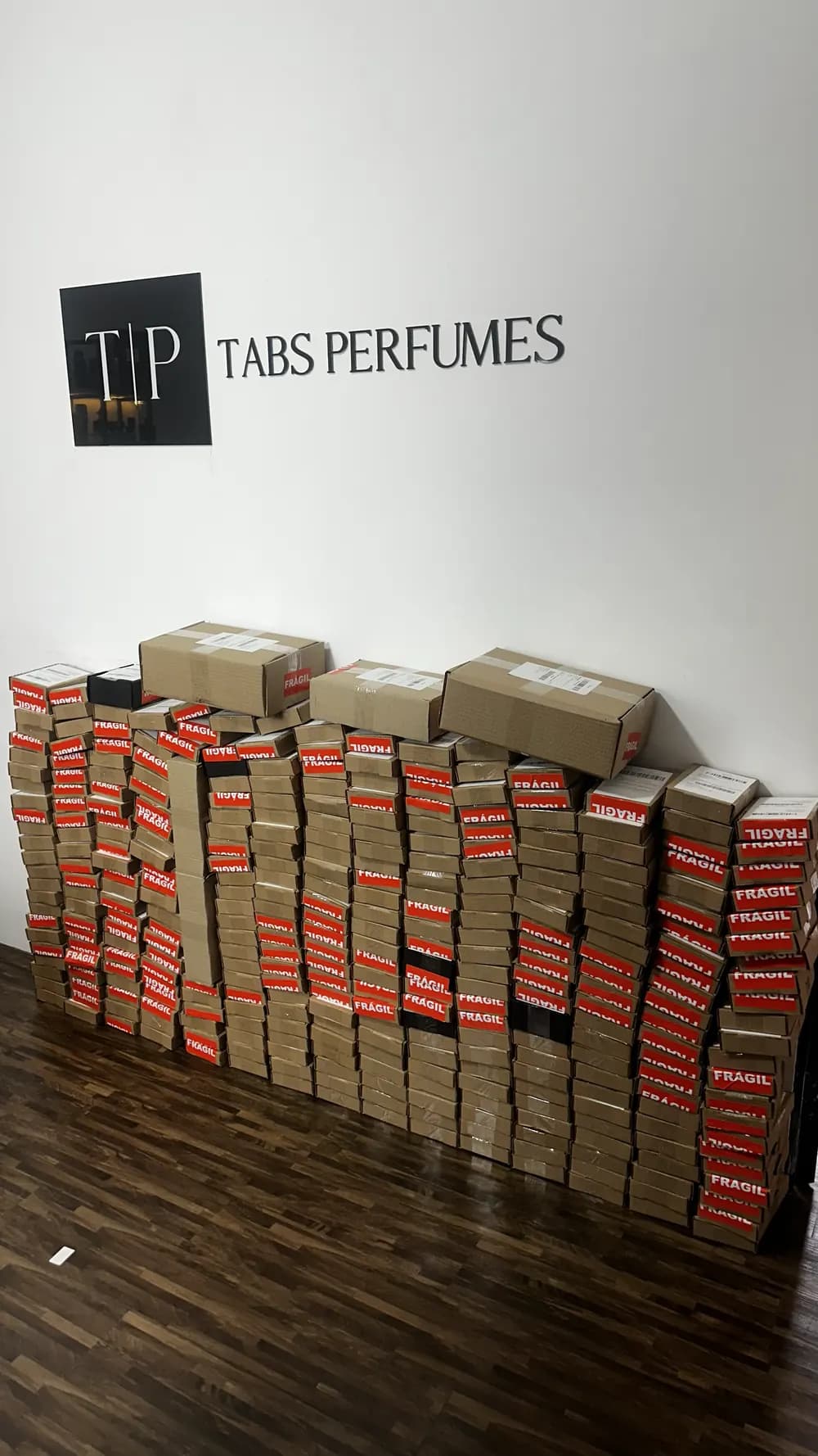 Parede de caixas de pedidos embaladas no escritório da Tabs, diante do logo Tabs Perfumes
